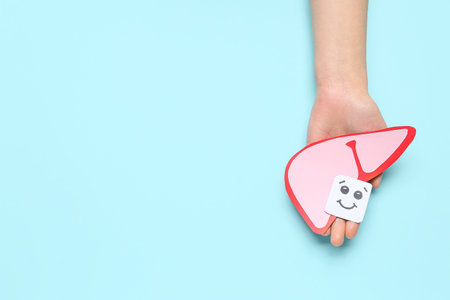 Female hand holding pink paper liver and smiling face on blue backgroundの写真素材