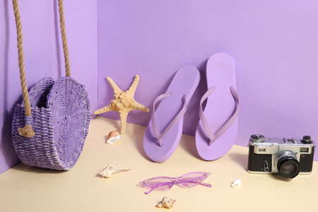 Flip flops with sunglasses, camera and bag on lilac backgroundの写真素材