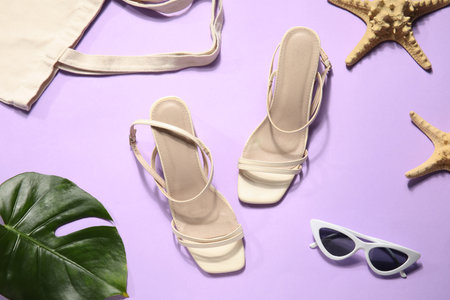 Pair of high heeled sandals with sunglasses and bag on lilac backgroundの写真素材