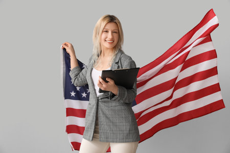 Young businesswoman with clipboard and USA flag on gray backgroundの写真素材