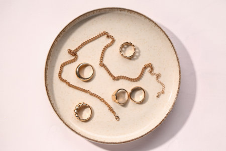 Plate with golden rings and necklace on white background
