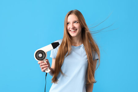 Beautiful young woman with hair dryer on light blue backgroundの写真素材
