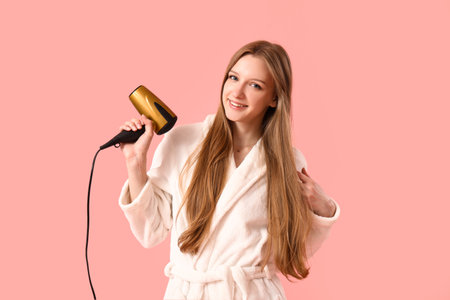 Beautiful young woman with hair dryer on pink backgroundの写真素材
