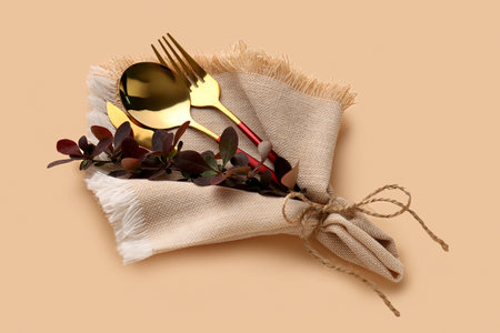 Golden cutlery with barberry twig in napkin on beige background