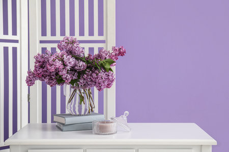 Vase with lilac flowers, books and candle on table in roomの写真素材