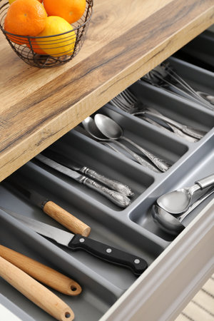 Open kitchen drawer with different silver cutlery and bowl of fruitsの写真素材