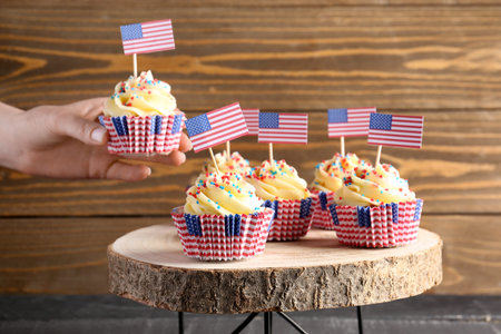Female hand with tasty patriotic cupcakes and flags of USA near brown wooden wall. american independence dayの写真素材