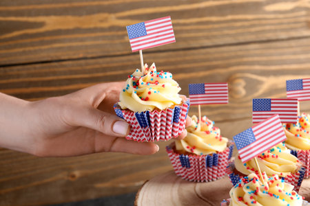 Female hand with tasty patriotic cupcakes and flags of USA near brown wooden wall. american independence dayの写真素材