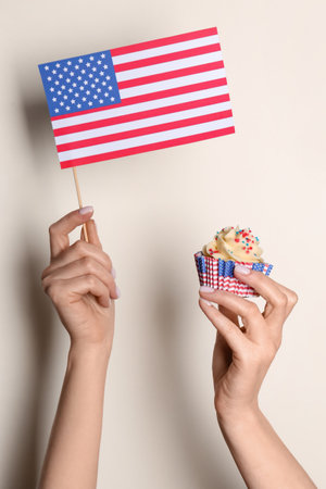 Female hands with tasty patriotic cupcake and USA flag near pale yellow wall. american independence dayの写真素材