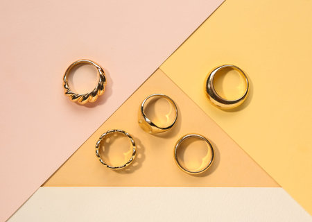 Different beautiful golden rings on color background