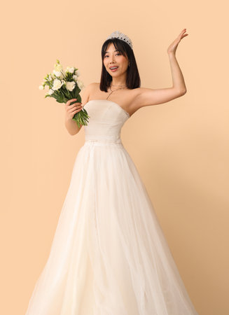 Beautiful young Asian bride with bouquet of eustoma flowers on beige backgroundの写真素材