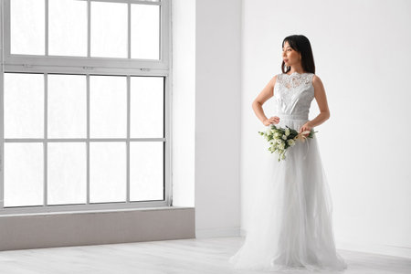 Beautiful young Asian bride with bouquet of eustoma flowers in roomの写真素材