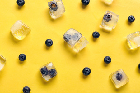 Ripe blueberry frozen in ice cubes and fresh berries on yellow backgroundの写真素材
