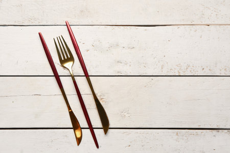 Golden fork and knives with red handles on white wooden backgroundの写真素材