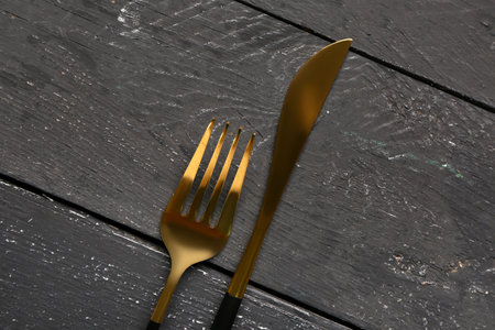 Golden fork and knife with on black wooden backgroundの写真素材