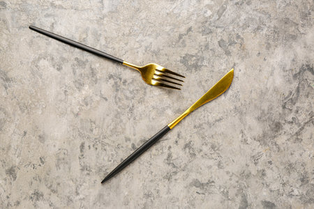 Golden fork and knife with black handles on gray backgroundの写真素材
