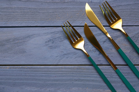 Golden forks and knives with colored handles on blue wooden backgroundの写真素材