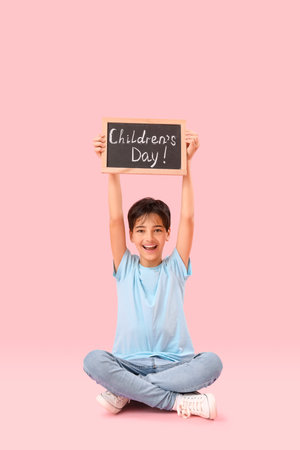 Little boy holding chalkboard with text CHILDREN'S DAY on pink backgroundの写真素材
