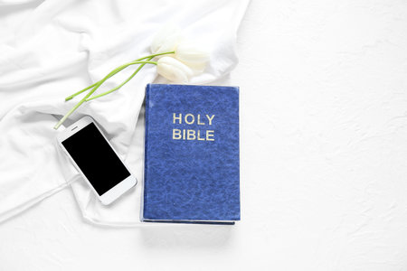 Holy Bible with tulip flowers and smartphone on white textured background