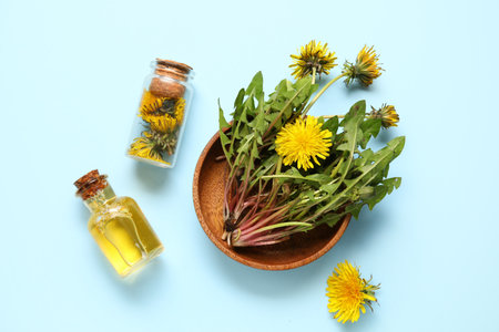 Bottles with cosmetic oil and bowl of dandelion flowers on blue backgroundの写真素材