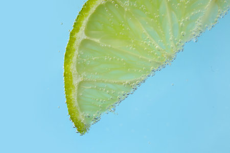 Lime slice in water with bubbles on blue backgroundの写真素材