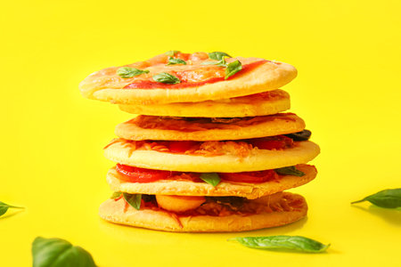 Tasty mini pizzas with basil on yellow background