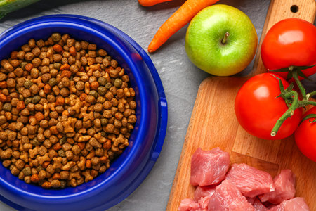 Bowl with dry pet food, raw meat and natural products on color wooden background, closeup