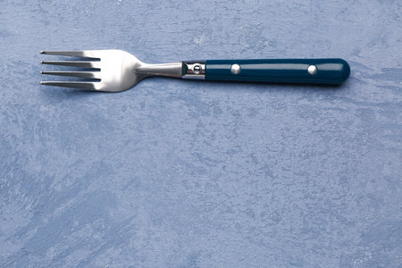 Stainless steel fork with plastic handle on grunge blue background