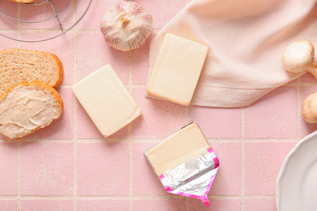 Processed cheese, bread and vegetables on pink tile backgroundの写真素材