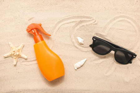 Creative composition with spray bottle of sunscreen cream and sunglasses on sand
