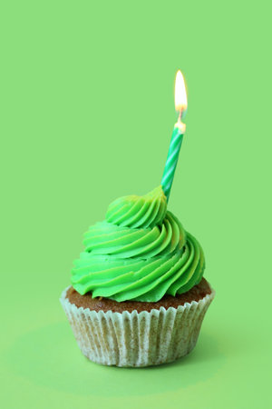 Tasty cupcake with birthday candle on green backgroundの写真素材