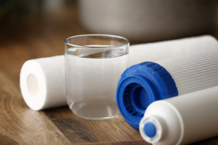 Glass of water with filters on wooden table in kitchen