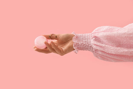 Hand holding jar of cosmetic cream on pink backgroundの写真素材