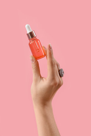 hand holding cosmetic product on pink backgroundの写真素材
