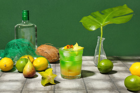 Fresh summer cocktail with carambola and flower on tile table near green wallの写真素材