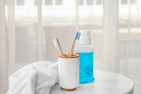 Holder with bamboo toothbrushes, rinse and towel on table in roomの写真素材