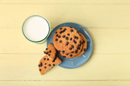 Tasty cookies with chocolate chips and glass of milk on yellow wooden backgroundの写真素材