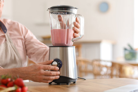Mature man making fruit smoothie with blender in kitchen, closeupの写真素材