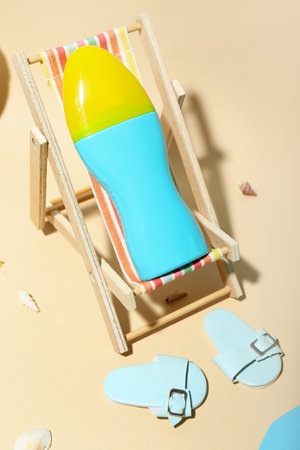 Creative composition with miniature deckchair and sunscreen on the beach