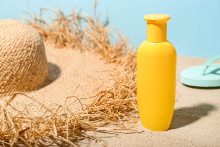 Creative composition with sunscreen cream, summer hat and flip flops on sand