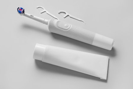 Electric toothbrush with paste and toothpicks on gray background