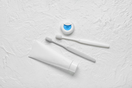 Dental floss with toothbrushes and paste on textured white background