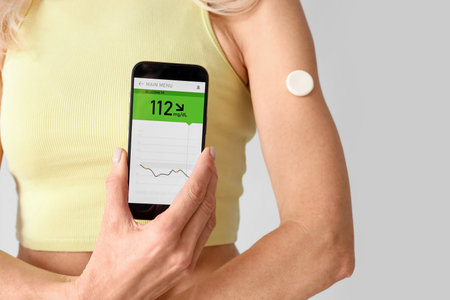 Mature diabetic woman with mobile phone measuring blood sugar level on light background, closeupの写真素材
