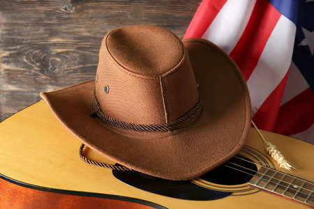 Cowboy hat, guitar and flag of USA on wooden background