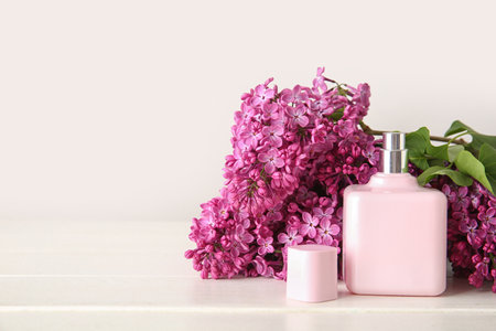 Beautiful blossoming lilac flowers with bottle of perfume on wooden table near white wallの写真素材