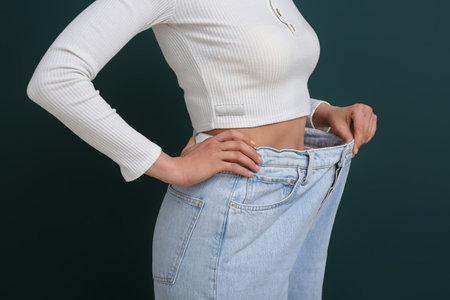 Young woman in loose jeans on green background. Diet conceptの写真素材