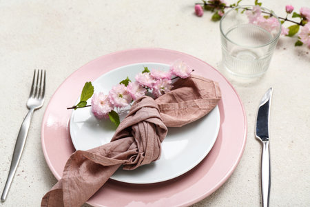 Beautiful table serving with cutlery, blooming tree branches and folded napkin on white grunge...