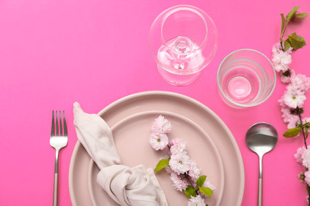 Beautiful table serving with cutlery, blooming tree branches and folded napkin on pink backgroundの写真素材