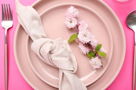 Beautiful table serving with cutlery, blooming tree branch and folded napkin on pink backgroundの写真素材