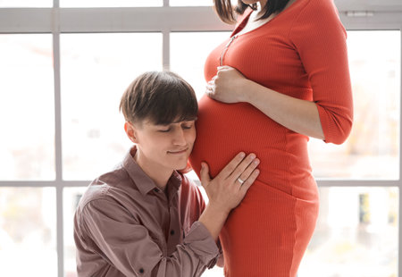 Young pregnant couple near window at homeの写真素材